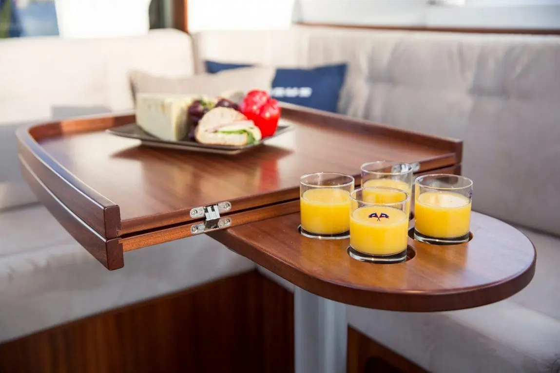 A wooden table holds glasses of orange juice and a platter with a sandwich, cheese, and vegetables in a modern interior setting.